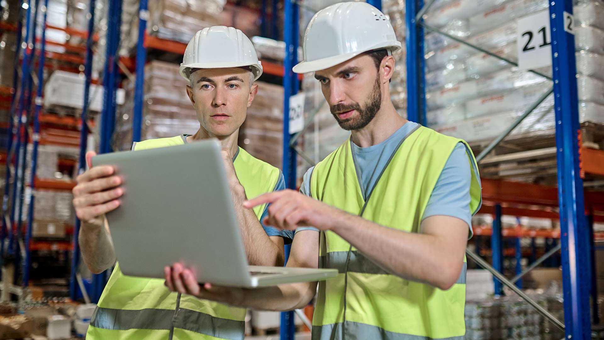 Manufacturing supervisors using QMS software on a laptop in a warehouse to manage quality control and certification processes.