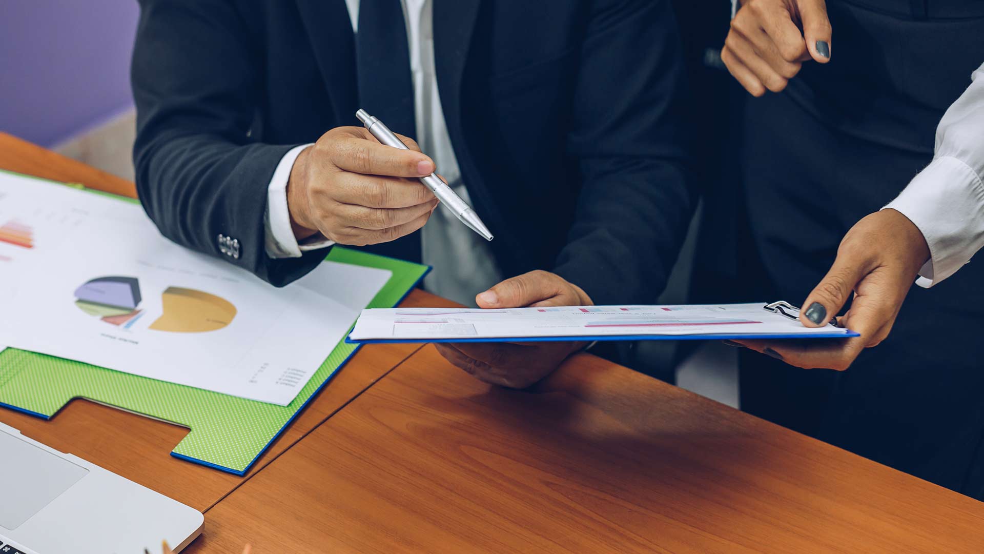 Two business professionals closely reviewing and pointing at data charts and documentation on a clipboard and desk, illustrating a quality management legal audit.