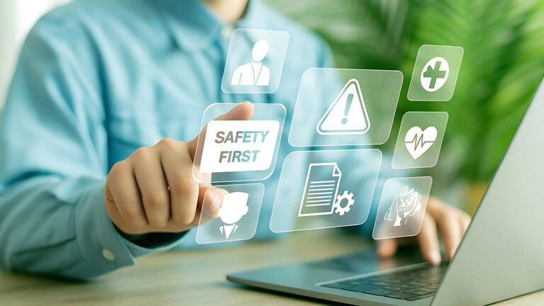 A professional pressing a digital button labeled "Safety First" on an interactive interface displaying health and safety icons next to a laptop.