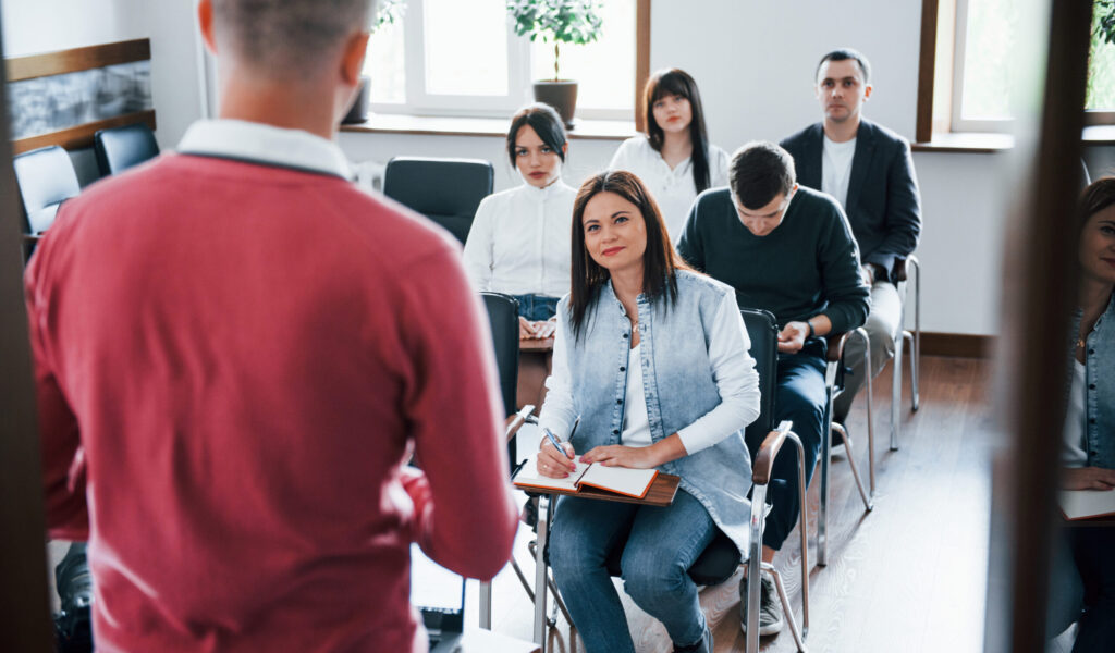 In red shirt. Group of people at business conference in modern classroom at daytime.